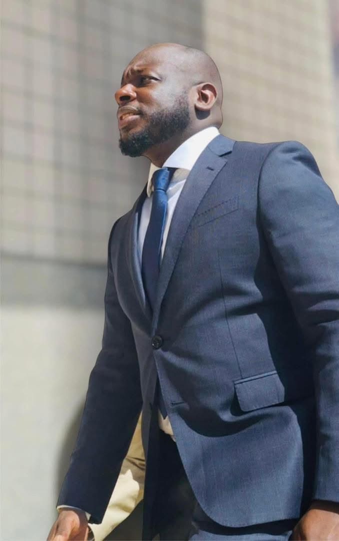 Bakary DIABY en costume gris, en marche, le regard déterminé