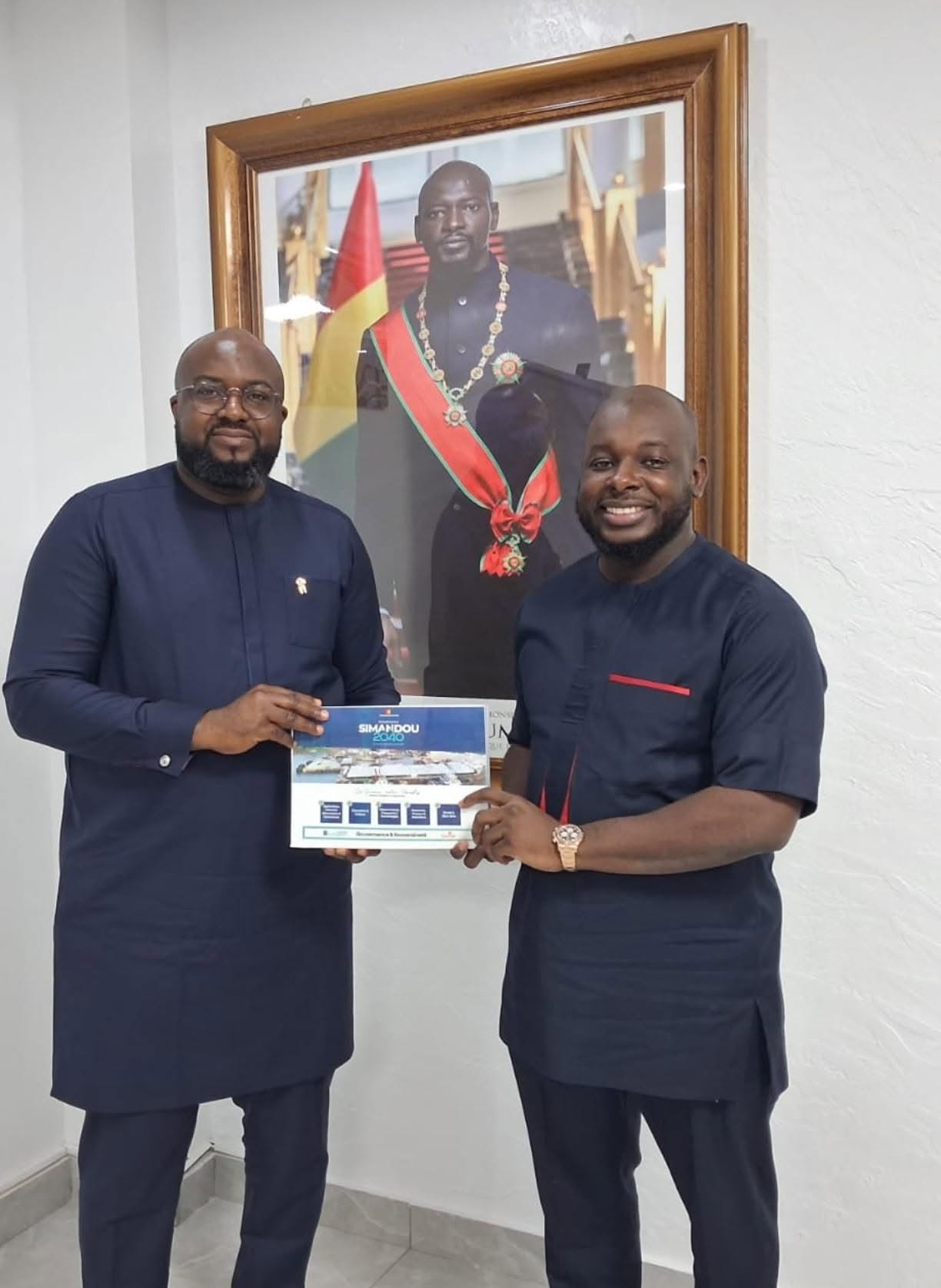 Bakary DIABY et le Ministre Djiba Diakité tenant ensemble le document « Simandou 2040 », devant le portrait officiel du Président Mamadi Doumbouya